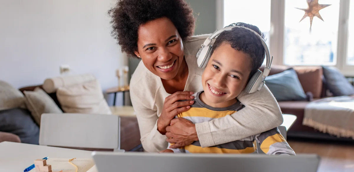 Mother and son smiling at the camera while working on their laptop