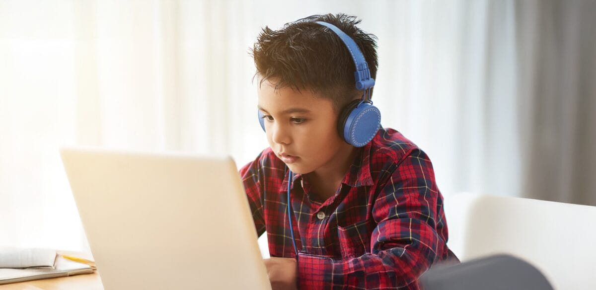 Elementary student attending to an online class wearing light blue headphones